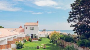 Una casa moderna con un césped cuidado, un pequeño patio con sillas y vista al mar.
