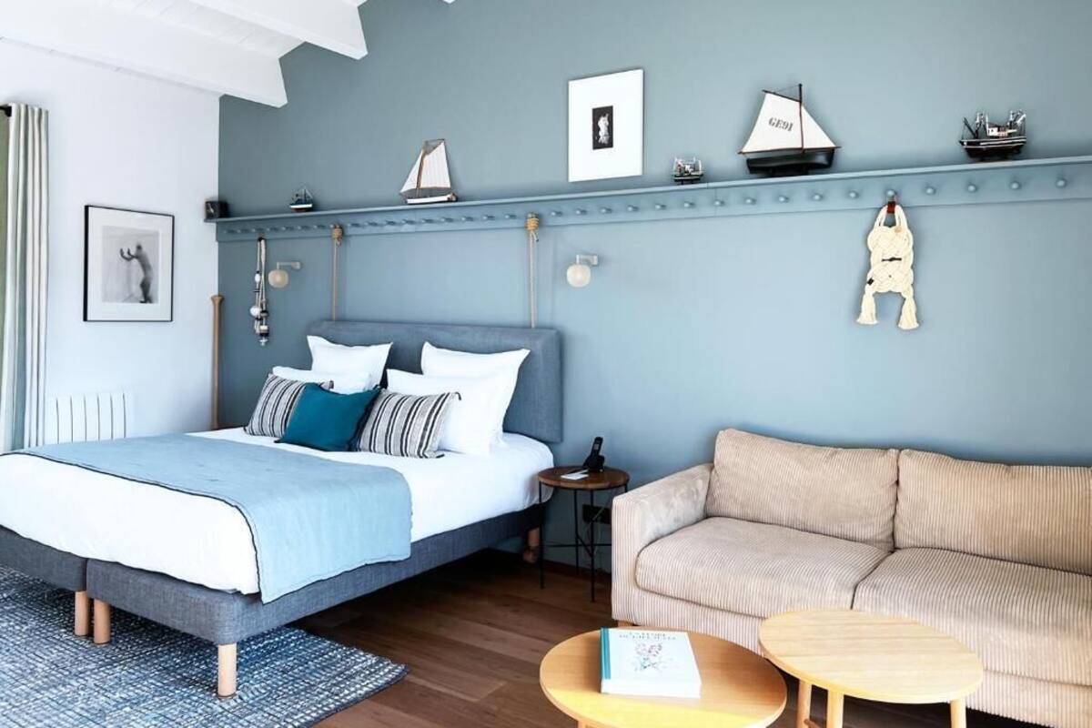 A bedroom with a bed, a sofa, a small table, and a shelf with decorative items.