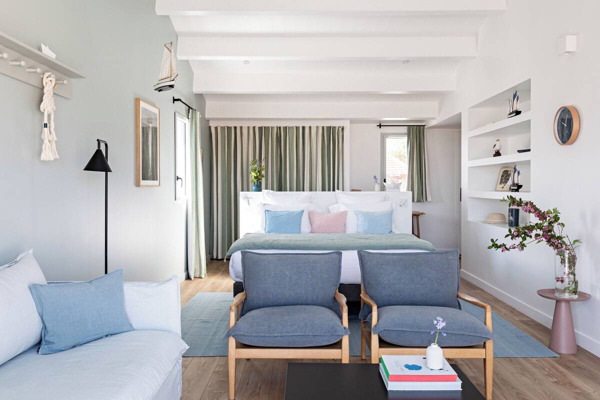 A modern bedroom with a large bed, two armchairs, a sofa, and a bedside table with books.