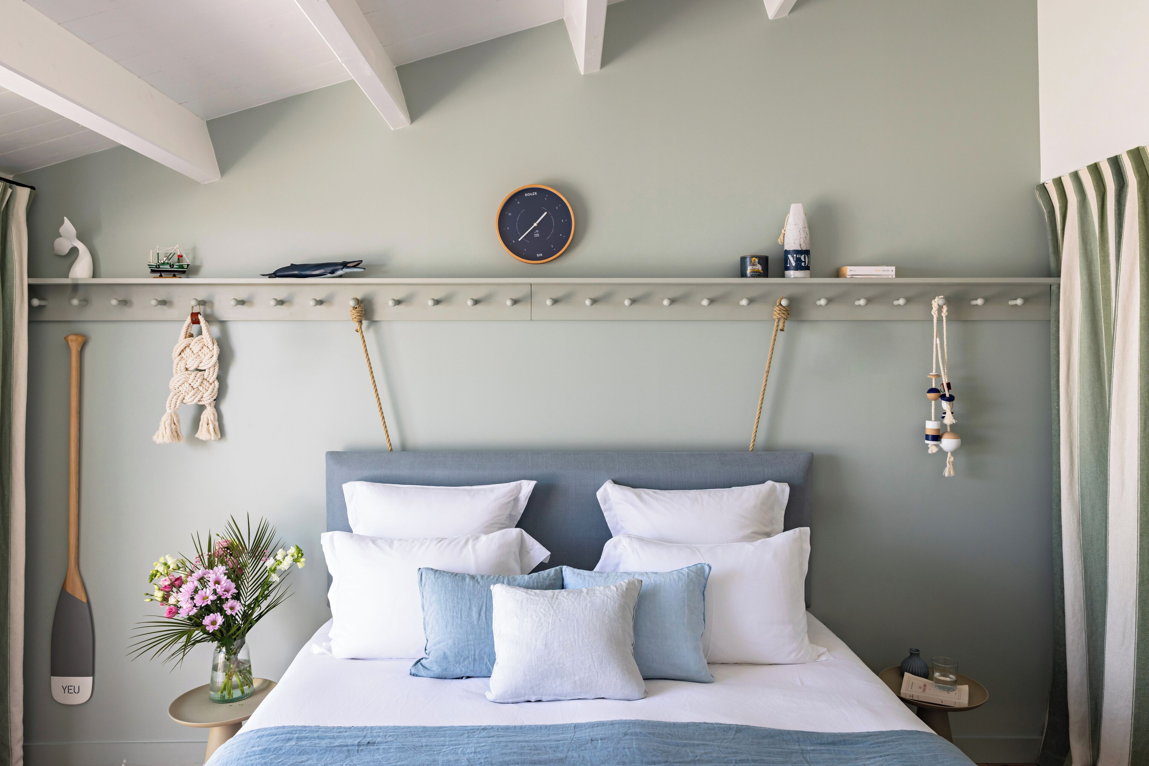 A neatly arranged bedroom with a bed, pillows, a clock, and a small shelf with decorative items.