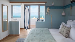 Un dormitorio con una cama, una ventana con vista al mar y una tabla de surf apoyada en la pared.