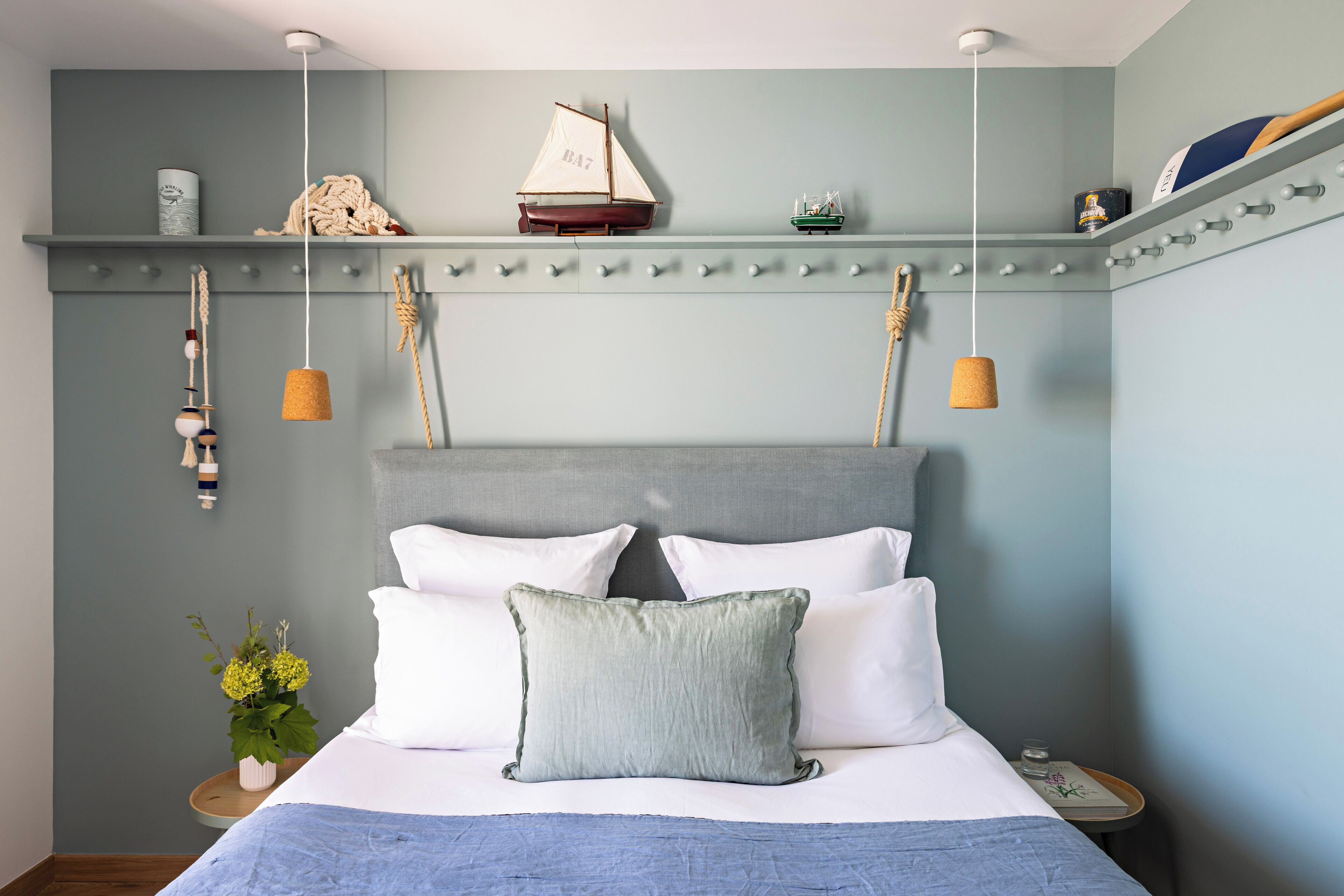 Un dormitorio ordenado con cama, almohadas, una estantería con objetos decorativos y una lámpara colgante.