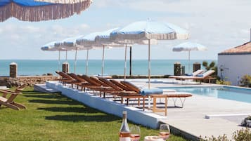 Zona de piscina con sillas reclinables, sombrillas y una mesa de comedor con una botella de vino.