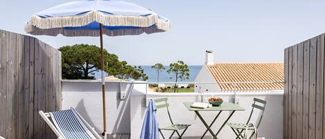 A wooden deck with a lounge chair, a table with chairs, and an umbrella.