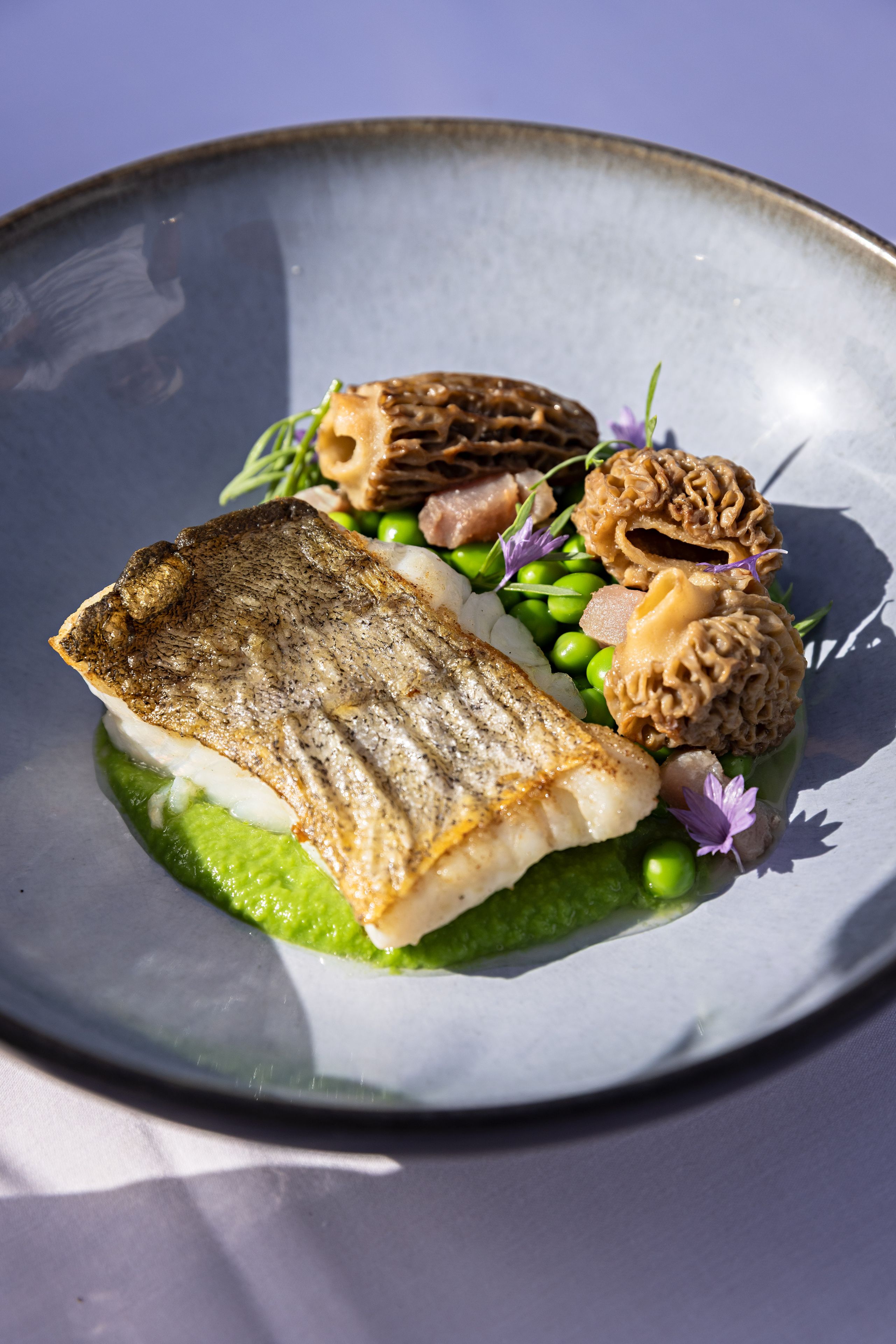 Une assiette contenant un morceau de poisson, des petits pois et une sauce verte.