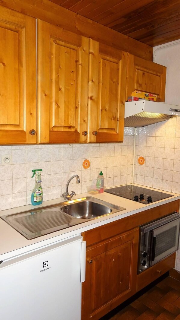 A kitchen with wooden cabinets, a stainless steel sink, a white countertop, a dishwasher, and an oven.