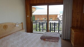 A bedroom with a bed, a wooden headboard, a window with a view of buildings and a fence, and a wooden dresser.