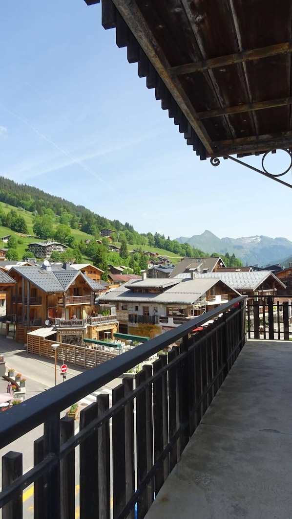 A balcony with a view of a village, wooden buildings, and mountains in the background.