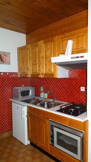 A compact kitchen with wooden cabinets, a microwave, a sink, a stove, and a small refrigerator.