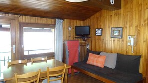 A wooden interior with a dining table, chairs, a sofa, a television, and a telephone.