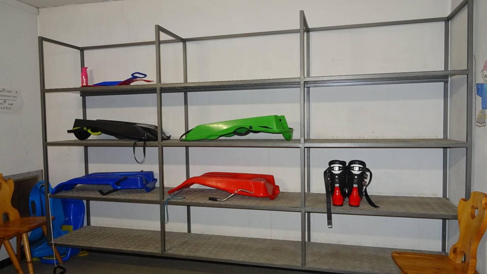 A metal shelving unit with various items on it, including a green object, a red object, and two black objects.
