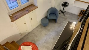 Ein modernes Wohnzimmer mit einer Holzbank, einem blauen Sessel, einem kleinen Hocker und einem Standventilator.