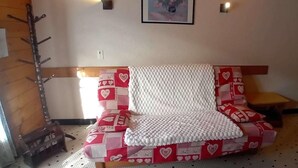 Een kamer met een bank bedekt met een geborduurd plaid, een houten kapstok, een klein tafeltje en een wandlamp.