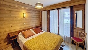 Een kamer met houten lambrisering, een bed, nachtkastje, stoel en een raam met gordijnen.