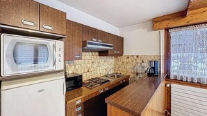 Een kleine keuken met houten kastjes, een magnetron, een kookplaat en een spoelbak.