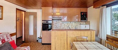 A compact room with a kitchenette, a sofa, a bed, and a window with a view.