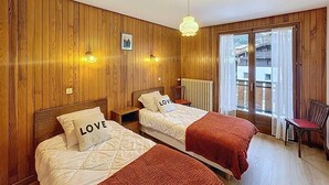 A room with two beds, wooden paneling, a radiator, a window with curtains, and a chair. - Wifi, 2nd floor, terrace, balcony, parking, 50m², Les Gets (Les Gets)