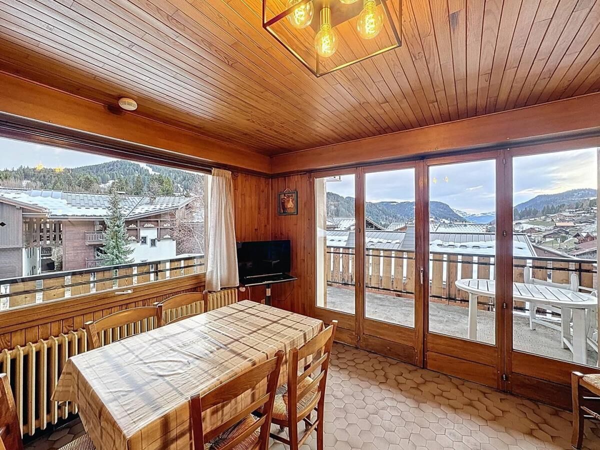 Un intérieur en bois comprenant une table et des chaises, un téléviseur et de grandes fenêtres donnant sur des bâtiments et des montagnes.