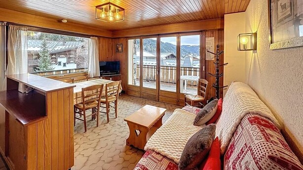 A cozy room with wooden walls and ceiling, a sofa with patterned cushions, a wooden table, and a TV. - Wifi, 2nd floor, terrace, balcony, parking, 50m², Les Gets (Les Gets)
