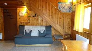 Interior em madeira com um sofá, uma mesa pequena, uma escada e um relógio fixado na parede.