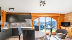 A modern kitchen with dark cabinets, a dining area with a table and chairs, and a large window offering a mountain view. - Wifi, Ground floor, view mountain, terrace, parking, tv, 40m², Les Gets (Les Gets)
