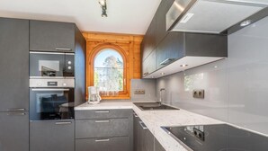 A modern kitchen with dark cabinetry, a built-in oven, a coffee maker, and a large window with a view of trees. - Wifi, Ground floor, view mountain, terrace, parking, tv, 40m², Les Gets (Les Gets)