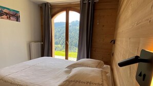 A bedroom with a bed, a window with curtains, and a view of a forest. - Wifi, Ground floor, view mountain, terrace, parking, tv, 40m², Les Gets (Les Gets)
