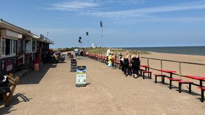 Une promenade en bord de mer, avec des bancs rouges, un vendeur de nourriture et une enseigne indiquant qu'on y vend de la glace artisanale à base de lait frais.