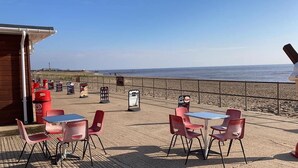 Un café situé en bord de mer, avec des tables et des chaises, un bâtiment en bois et une vue sur l’océan.