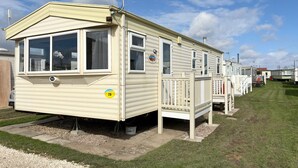 Une rangée de maisons mobiles, avec une pelouse verdoyante, un ciel dégagé et une petite terrasse attenante à l’une des maisons.