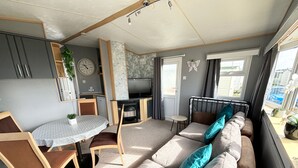 Un espace de vie compact comprenant un canapé, une table à manger, des chaises, un petit coin cuisine et une cheminée.