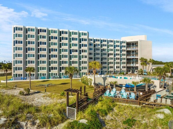 Un hotel moderno con varios pisos, un área de piscina con tumbonas y vista al mar.