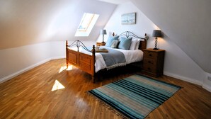 Un dormitorio con una cama de madera, una mesita de noche, una lámpara, una ventana y un cuadro en la pared.