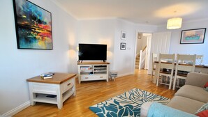 Una sala de estar con televisor de pantalla plana, mesa de centro de madera y alfombra estampada.