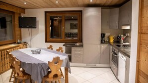 Une cuisine de taille réduite, dotée de meubles en bois, une table à manger avec des chaises, un téléviseur fixé au mur et une fenêtre offrant une vue agréable.