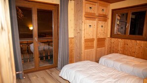 Une chambre de style cabane en bois, avec deux lits, une porte-fenêtre coulissante donnant sur un balcon et des lambris en bois sur les murs.