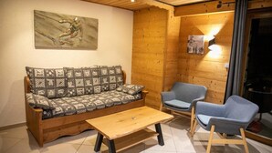 Une pièce chaleureuse avec un canapé en bois, deux fauteuils, une table basse en bois et un tableau accroché au mur.