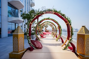 Arches adorned with floral decorations and golden lanterns lead to a formal event space with a red carpet.