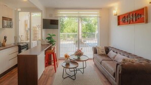 A modern living room with a brown leather sofa, a coffee table, and a kitchen area with a bar and red stools. - Golden Pucon 3BR (Pucon)