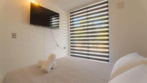 A bedroom with a bed, a mounted TV, and a window with blinds. - Golden Pucon 3BR (Pucon)