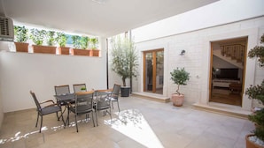 Une vaste terrasse dotée d’une table et de chaises, entourée de plantes en pot et d’un grand arbre.