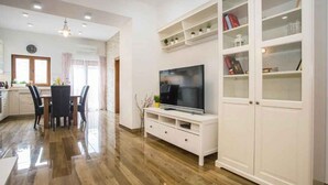 Ein modernes Wohnzimmer mit Flachbildfernseher, weißen Schränken und einem Essbereich mit Stühlen und einem Tisch.