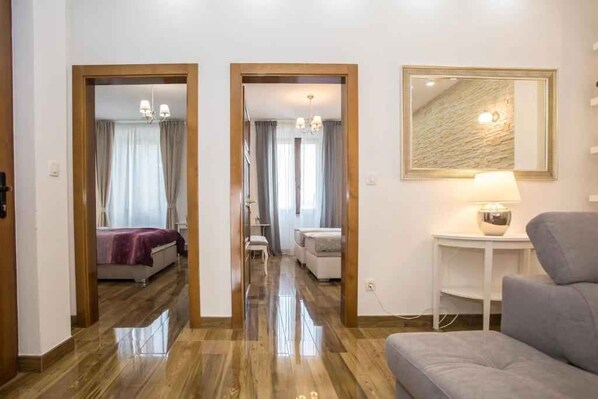 A hotel room with a wooden floor, a bed with a purple bedspread, a small table with a lamp, and a large mirror on the wall.