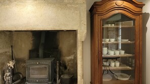 Una habitación con chimenea de piedra, estufa antigua y un aparador de madera con vajilla.