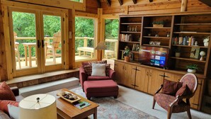 A cozy wooden interior with a sofa, armchair, and a TV displaying a streaming service interface. - Charming home in Seven Devils. Close access to tubing, ziplining, & hiking. (Seven Devils)