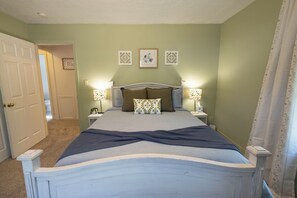 A bedroom with a bed, two bedside lamps, a door, and a wall with three framed pictures.