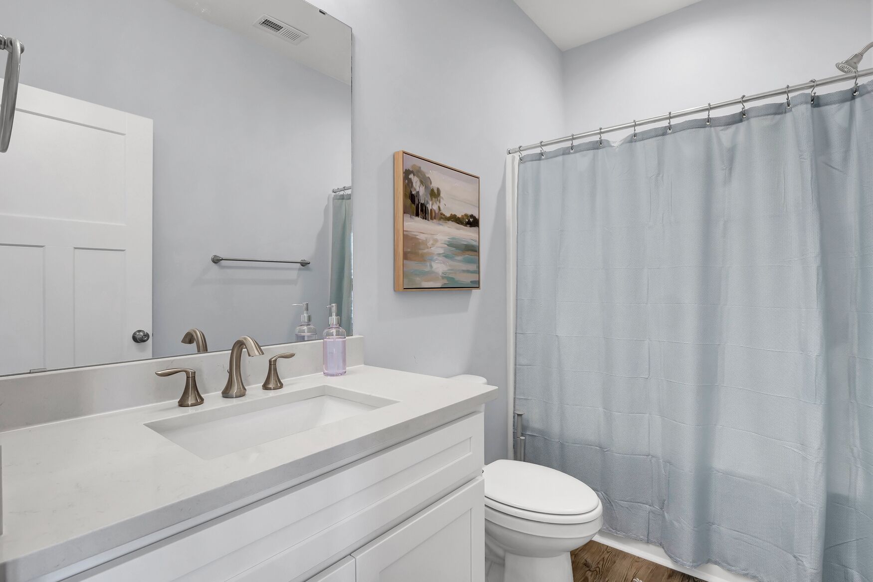 Un baño moderno con tocador blanco, un espejo grande, inodoro y cortina de ducha.
