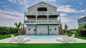 A two-story house with a balcony, a swimming pool, and a well-maintained lawn.
