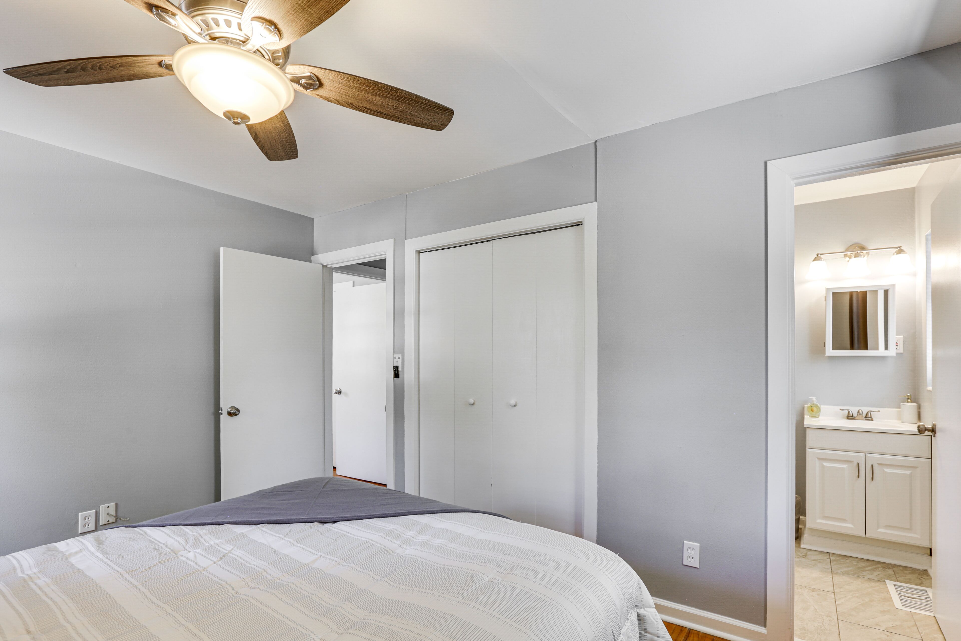 Un dormitorio con cama, ventilador de techo y puerta que da a un baño.