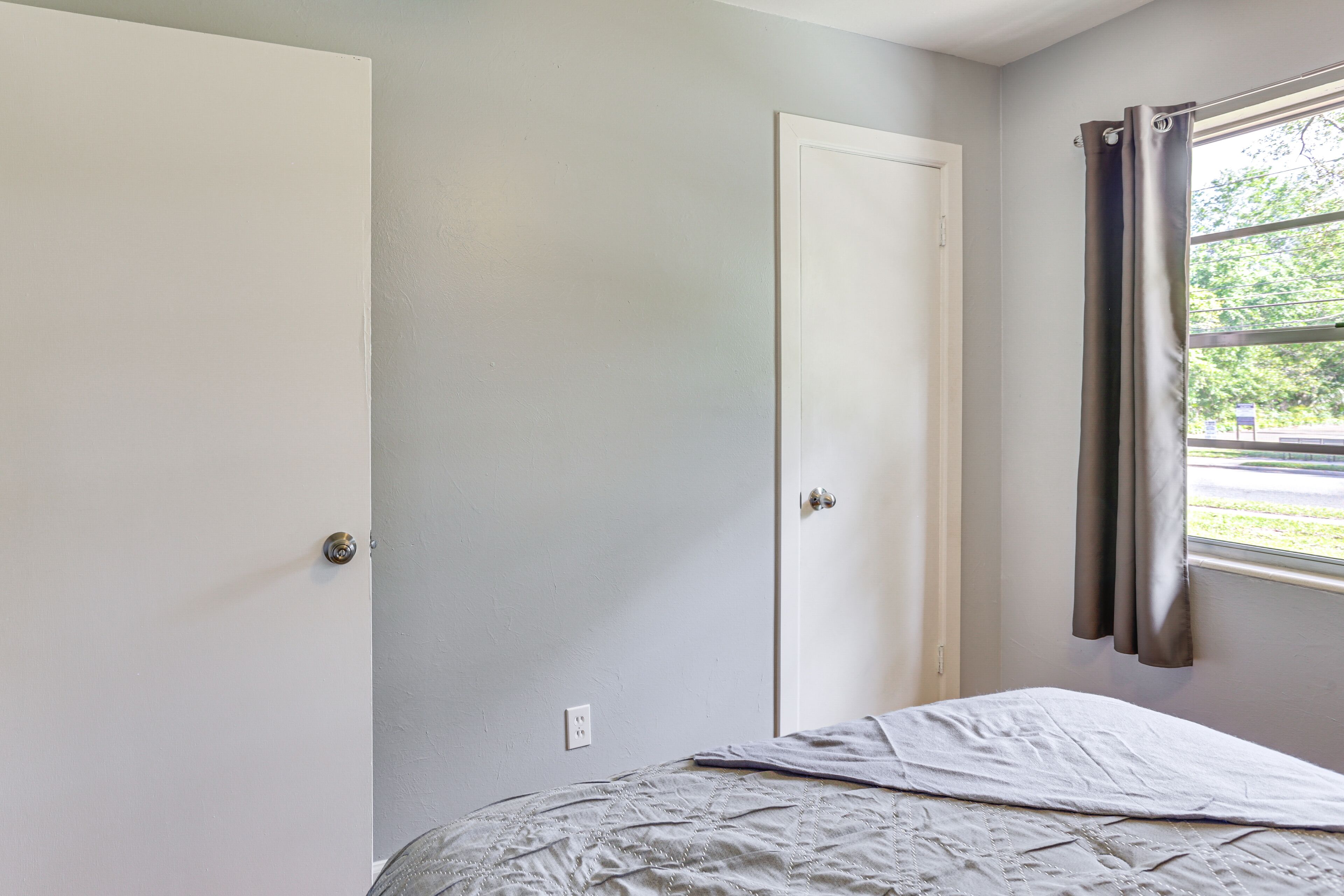 A bedroom with a bed, a door, and a window with curtains.